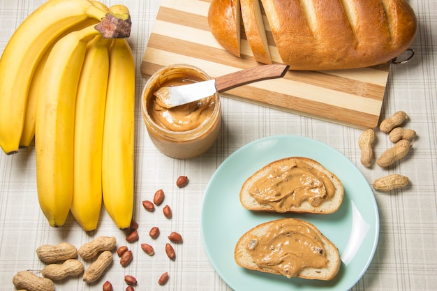 Making lunch, peanut butter sandwich. apples, bananas and a\
glass of milk in the background.