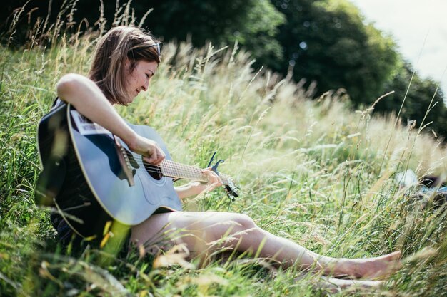 写真 屋外で音楽を作る 若い女の子が夏の川でギターを弾く