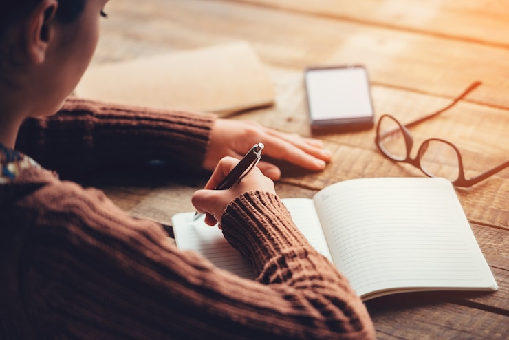 Photo making notes. close-up image of woman writing in notebook with copy space while sitting at the rough wooden table