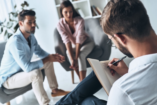 Making notes. Young married couple talking while sitting on the therapy session with psychologist