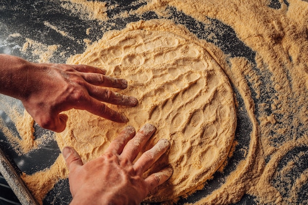 ピザ生地作り。テーブルの上で小麦粉を使って調理するピザの生地をこねる手