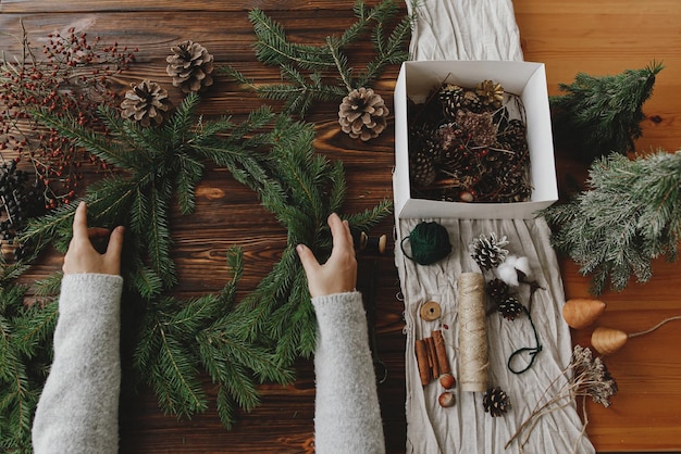 소박한 크리스마스 화환 만들기 나무 테이블에 녹색 전나무 가지를 들고 있는 손