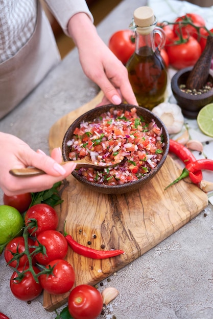 Making salsa dip sauce woman mixing chopped ingredients in wooden bowl