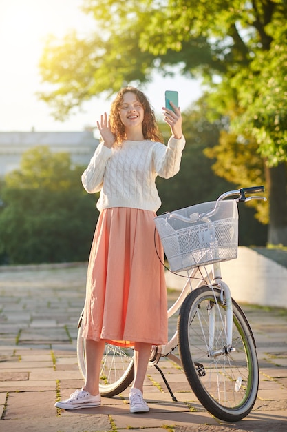 Making selfie. A dark-haired young girl with a bike making selfie in the park