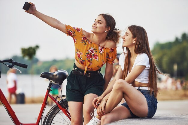 Making a selfie. Two young women with bike have a good time in the park.