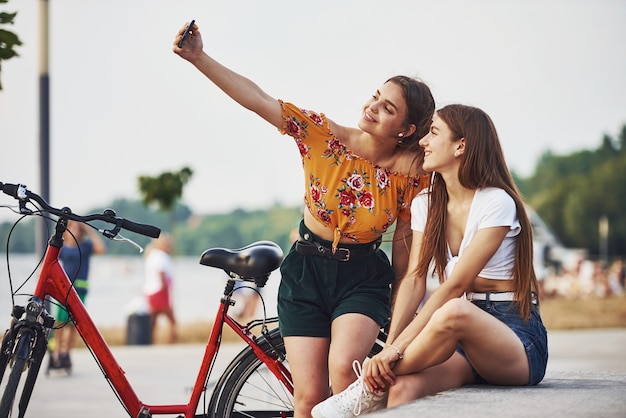 Photo making a selfie. two young women with bike have a good time in the park.