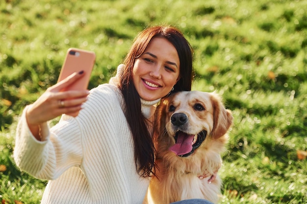 Making selfie Young woman have a walk with Golden Retriever in the park