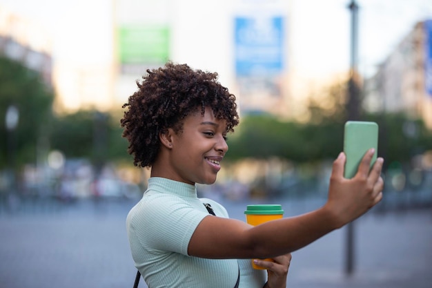 Making selfie Young woman with curly hair wearing fashionable clothes outdoors in the city