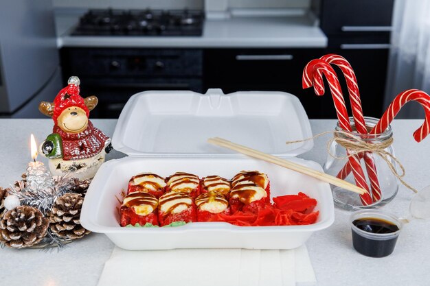 Making a set of Japanese baked rolls in a plastic box at home in the kitchen in a festive style Fast delivery sushi in a white container Christmas concept