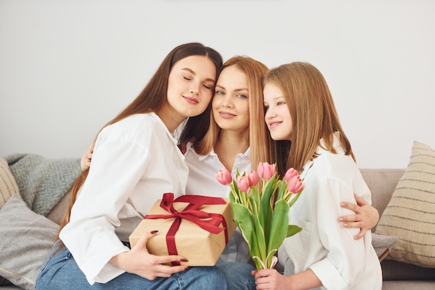 Making surprise with flowers Young mother with her two daughters at home at daytime