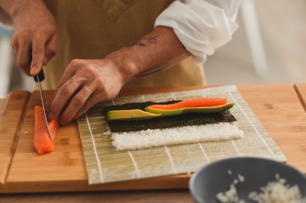 Making sushi process professional male chef in uniform slicing salmon fish preparing ingredients for