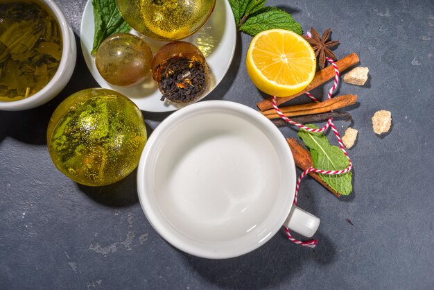 Making tea with trendy modern tea ball bombs. tea balls with
dried tea, cups, lemon and mint, with classic white cup, top view
copy space