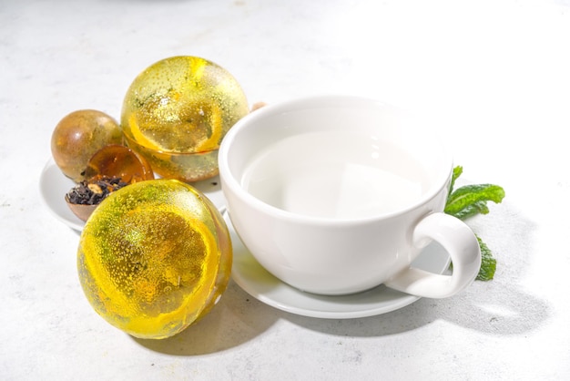 Making tea with trendy modern tea ball bombs. tea balls with\
dried tea, cups, lemon and mint, with classic white cup, top view\
copy space