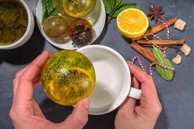 Making tea with trendy modern tea ball bombs tea balls with\
dried tea cups lemon and mint with classic white cup top view copy\
space