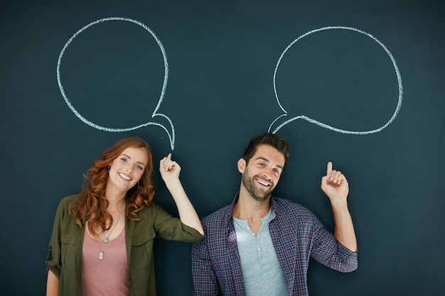 Making themselves heard Portrait of a young couple standing in front of a blackboard with speech bubbles drawn on it