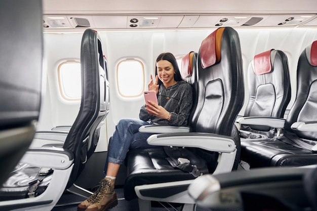 Making video connection Young woman in casual clothes sits on the passenger seat in the plane