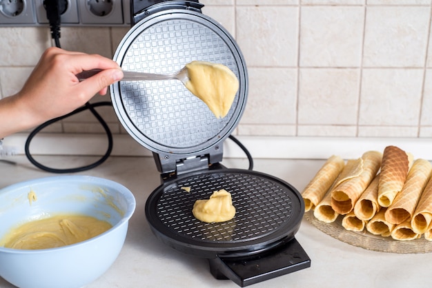 Making waffles at home - waffle iron, batter in bowl and ingredients - milk, eggs and flour. Cooking background.