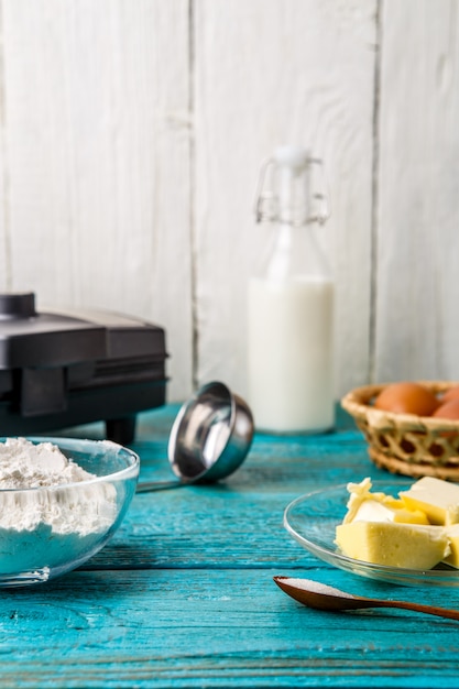 Making waffles at home - waffle iron and ingredients - milk, eggs and flour.