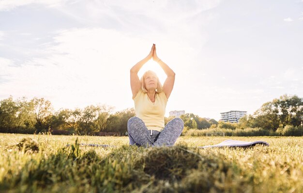 Making yoga exercises senior woman having nice weekend outdoors\
on the field at sunny day