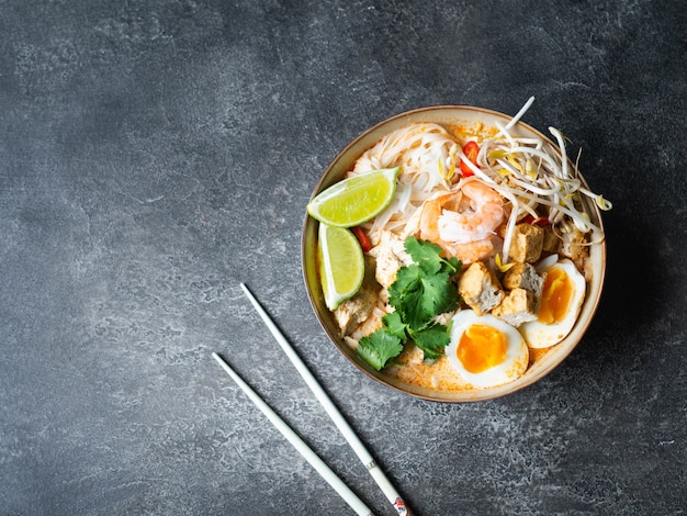 Malaysian noodles laksa soup with chicken, prawn and tofu in a bowl on dark surface