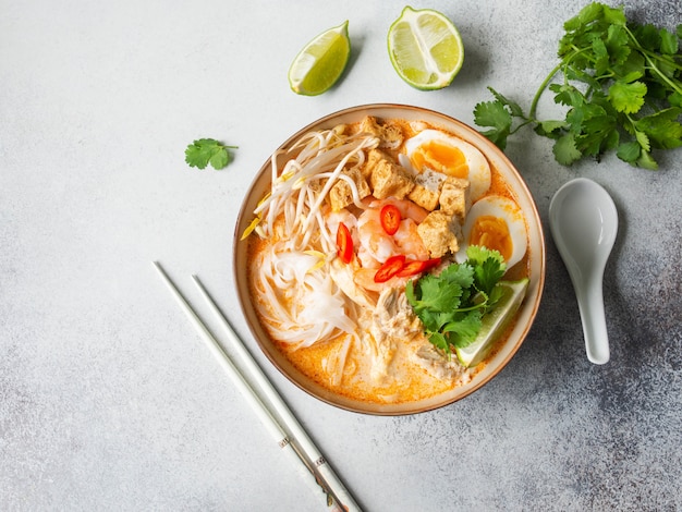 Malaysian noodles laksa soup with chicken, prawn and tofu in a bowl on grey surface