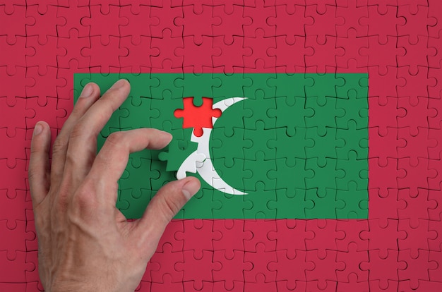 Maldives flag  is depicted on a puzzle, which the man's hand completes to fold