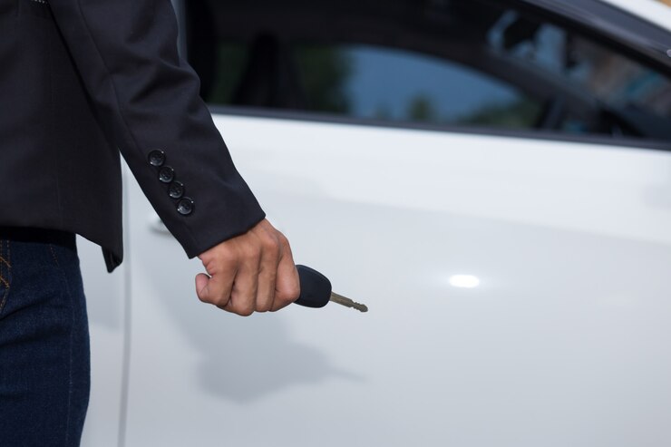 Male adult businessman in a suit  and holding a car key in his hand . White cars at the background