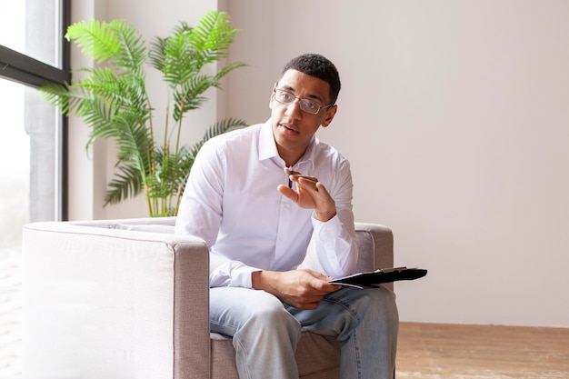 Male african american psychologist in armchair consults and tells session with psychotherapist