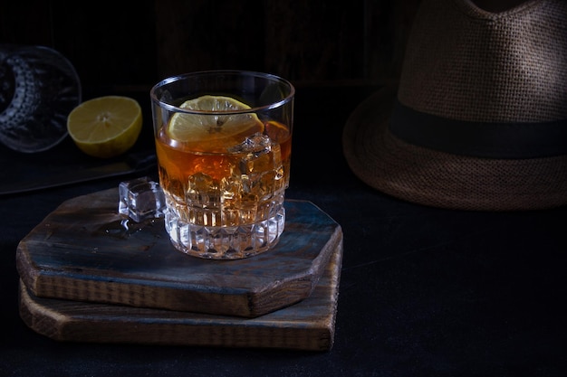 Male alcoholic drink rum whiskey on a dark wooden board with ice and lemon slices