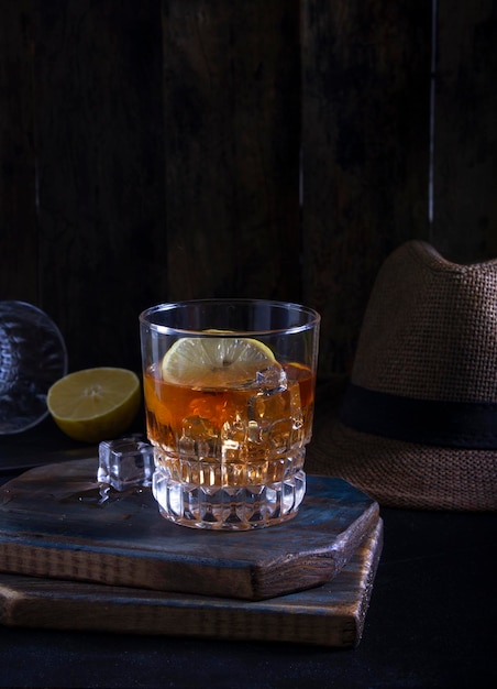 Male alcoholic drink rum whiskey on a dark wooden board with ice and lemon slices