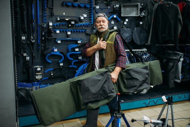 Male angler holds big case for fishing-rods in fishing shop.