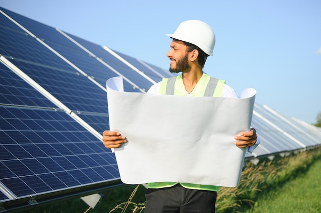 Male arab engineer standing on field with rows of solar panels