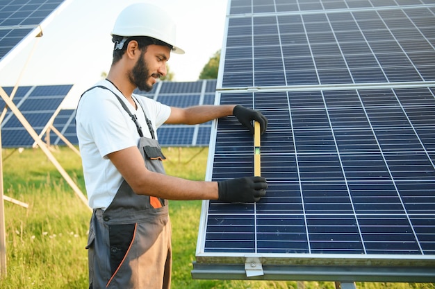 Male arabian engineer in helmet and brown overalls checking resistance in solar panels outdoors Indian man working on station