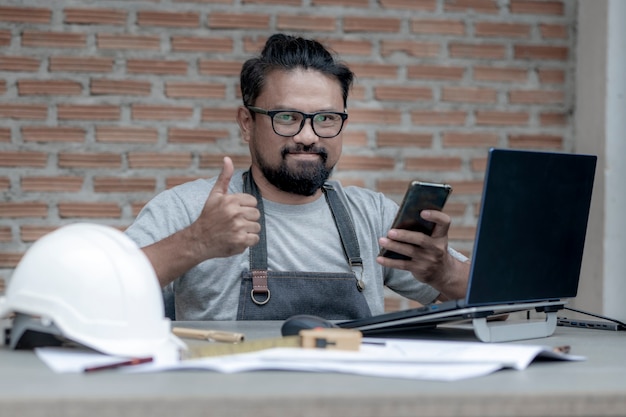 Male architect or engineer working at home drawing the construction project, An architect working on a laptop using a mobile phone on the working desk. Business and Technology concept.