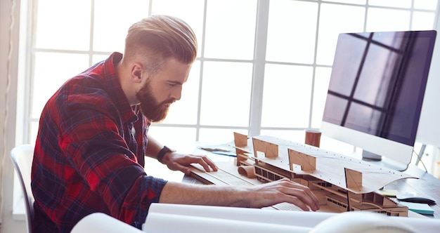 Male architect fixing details of wooden building model