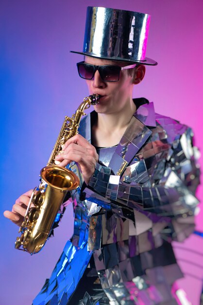 The male artist in a mirrored suit and a hat with a saxophone in neon light