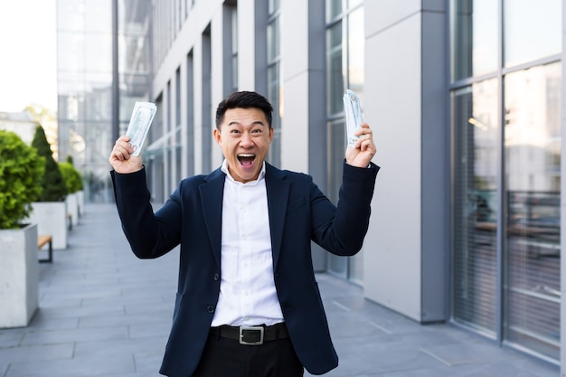 Male asian businessman rejoices holding a lot of cash dollars got a big win and payout