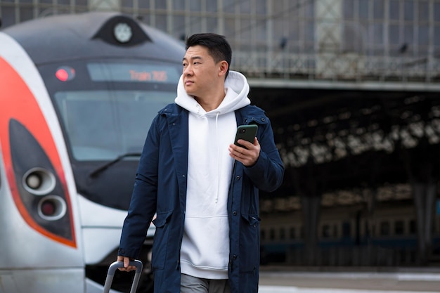 기차역에서 남성 아시아 사업가가 온라인으로 기차표를 사고, 휴대전화와 애플리케이션을 사용하고, 관광객은 출장에서 집으로 돌아온다