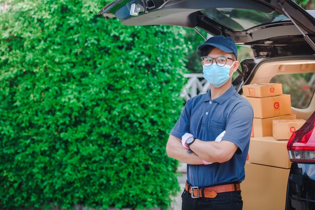 The male Asian delivery staff held a customer's paper box or box. The delivery workers wear protective masks and protective gloves.