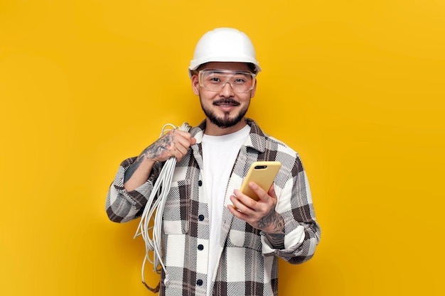 Male asian electrician in hard hat and glasses holds internet cable and phone