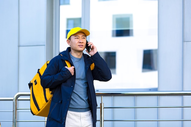 Мужчина-поставщик азиатской еды, идущий с курьером с большим рюкзаком для еды, разговаривает по телефону, узнает адреса доставки