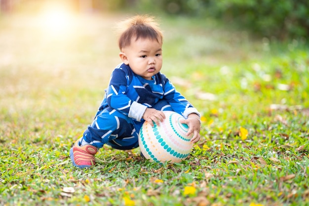 A male Asian kid holding and playing with a football in the outdoor backyard