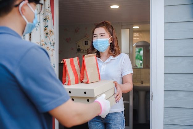 男性のアジアの荷主は、家の前にある美しい女性のクライアントに、フードデリバリーユニフォームに紙箱を入れて商品を配達しました。速達宅配サービスのコンセプト