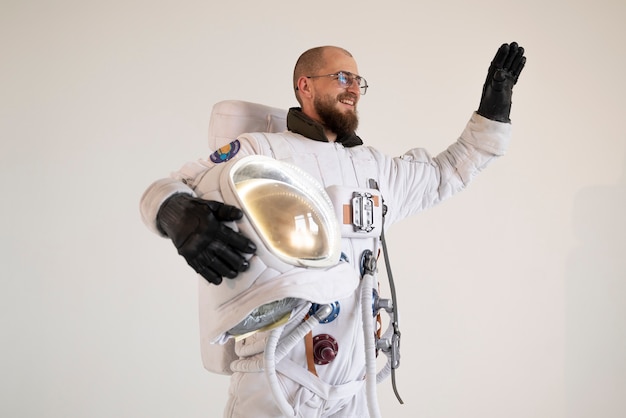 Мужчина-космонавт держит шлем и машет