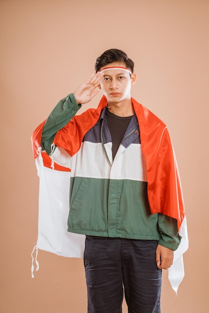 Male athelete from indonesia giving salute to indonesian flag proudly over isolated background