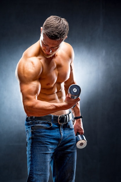 Male athlete bodybuilder holds dumbbell in hand. Pumping muscles. Naked torso.