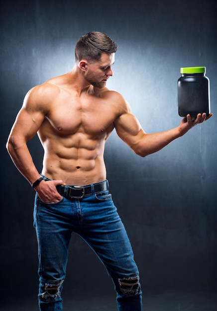 Photo male athlete bodybuilder with a naked torso stands with a jar of sports nutritional supplements