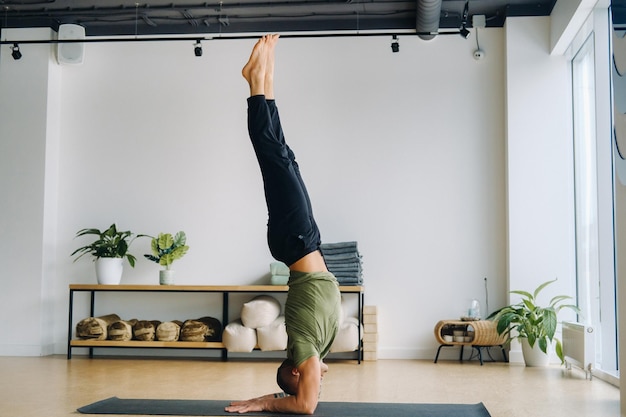 A male athlete in a green Tshirt Does Yoga in the gym