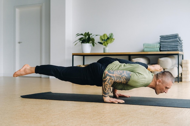 A male athlete in a green Tshirt Does Yoga in the gym