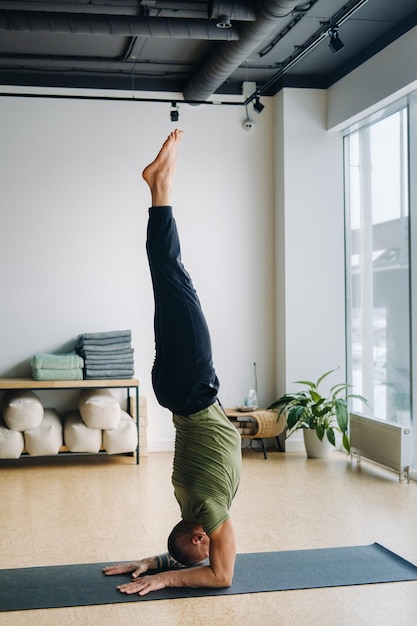 A male athlete in a green Tshirt Does Yoga in the gym